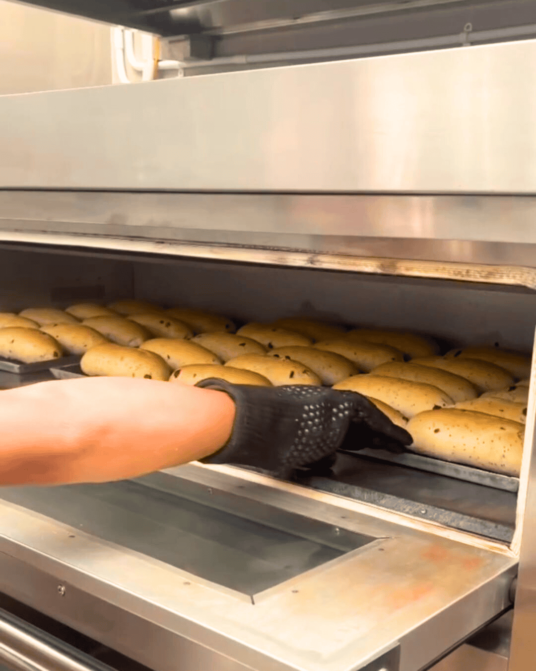 A person in a black shirt and gloves is putting bread in a oven